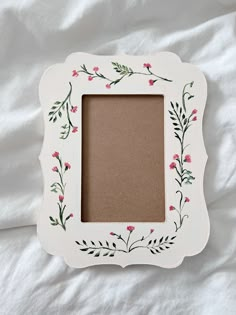 a white frame with pink flowers and leaves painted on the inside is sitting on a bed