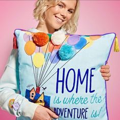 a woman holding a pillow with balloons on it and the words home is where the adventure begins