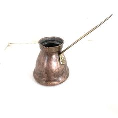 a small metal cup with a long handle and a stick sticking out of it's side