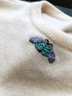 a white sweater with an embroidered bird on it