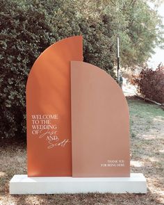 a large metal sculpture with writing on it in the middle of a field next to trees