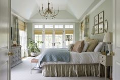 a large bed sitting under a chandelier in a bedroom next to a window