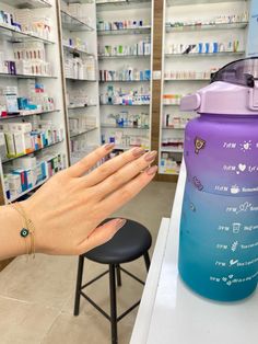 a person holding up a purple and blue water bottle in a pharmacy room with shelves full of medicines