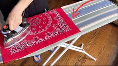 a person ironing on an ironing board with a red bandana and black iron