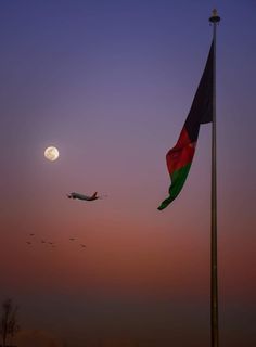 an airplane is flying in the sky at dusk with a flag and a full moon behind it