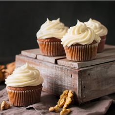 three cupcakes with white frosting sitting on top of a wooden box next to nuts