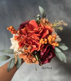 a bridal bouquet with orange and red flowers on it's arm, in front of a gray background