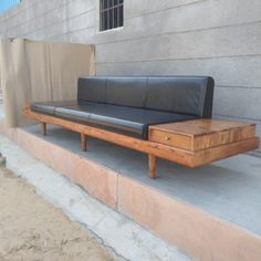 a black leather couch sitting on top of a wooden bench next to a cement wall