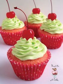 four cupcakes with green frosting and cherries on top are arranged in a row