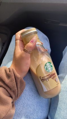 a woman is holding a starbucks drink in her hand while sitting on a car seat