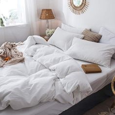 an unmade bed with white linens and pillows in a small room next to a window