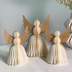 three white angel ornaments sitting next to each other in front of a vase with flowers