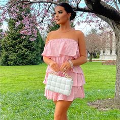 a woman in a pink dress is holding a white purse and posing for the camera