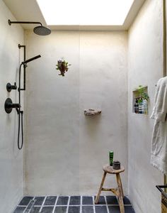 a bathroom with a walk in shower next to a wooden stool and towel rack on the wall