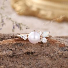 an opal and diamond ring on top of a piece of wood with flowers in the background