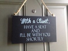 a sign hanging from the side of a door saying, with a client have a seat and i'll'll be with you shortly