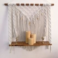 two candles are sitting on a shelf in front of a macrame wall hanging