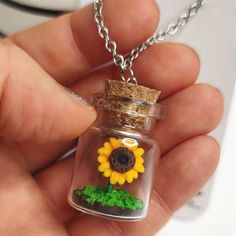 a hand holding a tiny glass jar with a sunflower in it and moss growing inside