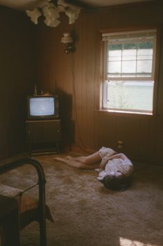 a person laying on the floor in front of a tv and a window with no curtains