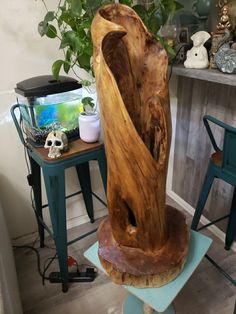 a large wooden sculpture sitting on top of a blue stool next to a potted plant