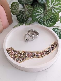 two wedding rings sitting on top of a white tray next to a green leafy plant