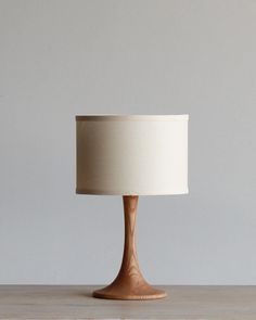 a wooden table with a white lamp on it and a gray wall in the background