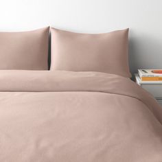 a bed with pink sheets and pillows on top of it next to a bookcase