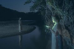 two people standing next to each other in front of a body of water at night