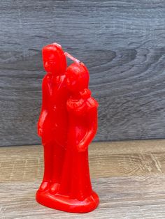 a red plastic figurine with two people holding each other on a wooden surface