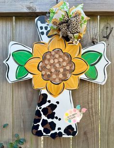 a wooden cross with a sunflower painted on the front and sides, attached to a fence