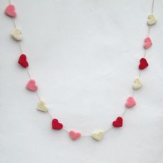 a necklace with hearts hanging from it on a white surface and red, pink, and yellow beads