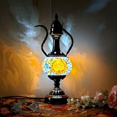 an ornate lamp is sitting on a table next to flowers and a wallpapered background