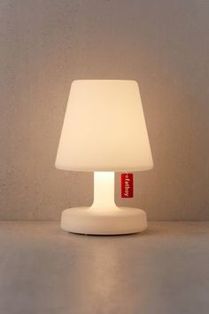 a white lamp with a red tag on it sitting in front of a gray wall