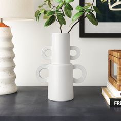 a white vase sitting on top of a table next to a lamp and a book