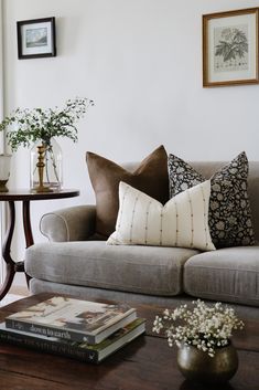 a living room filled with furniture and flowers on top of a wooden table next to a window