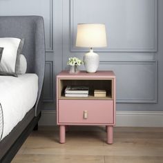 a pink nightstand next to a bed in a room with gray walls and wood flooring