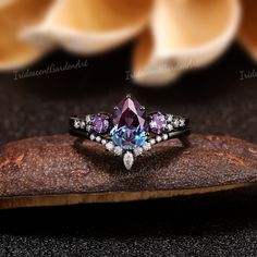 an image of a ring with purple and white stones in it on top of a piece of wood