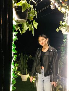 a woman standing in front of a potted plant next to a mirror with lights on it