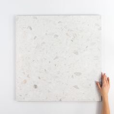 a person is holding up a white marble tile on the wall with their hand in front of it