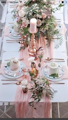 the table is set with pink and white plates, silverware, candles and flowers