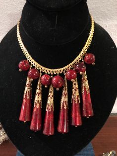 This lovely exotic necklace is pure drama. There are seven (7) round beads in a dark red (has a brownish tone)lacquer attached to the long gold tone metal chain. This chain is an unusual design loop off the base chain. Between each of these beads are long cylinder red lacquer bead topped with ornate gold tone metal filigree caps. This necklace slips over the head but also fastens with a lobster which dates it to the 1980s. The total length of the necklace is 30.5 inches and the long beads is jus Exotic Necklace, Design Loop, Red Lacquer, Bib Necklaces, Beaded Top, Unusual Design, Beaded Dangles, Gold Tone Metal, Metal Chain