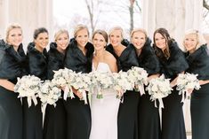 a group of women standing next to each other wearing black dresses and fur stoles