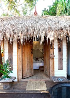 an outdoor hot tub in front of a thatched roof hut with a bed and bathtub