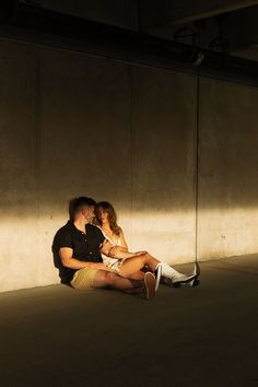 a man and woman sitting on the ground in an empty room with their arms around each other