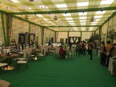 people are standing around tables and chairs in a room that has green carpet on the floor