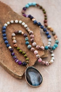 three necklaces with different colored beads on top of a stone slab next to a rock