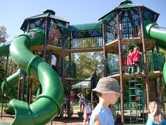 children are playing in the playground with green slides and climbing structures on each side of the slide