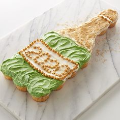 there is a green frosted cupcake on the marble platter that has been decorated with icing and sprinkles