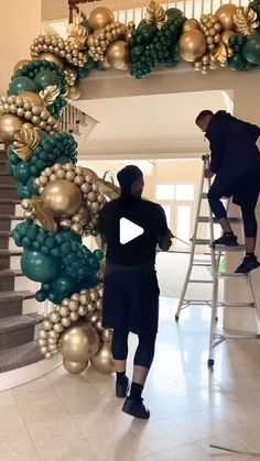 two men are decorating a christmas tree with gold and green ornaments on the stairs