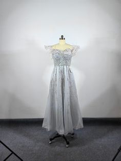 a white dress on a mannequin stand in front of a white wall and grey carpet